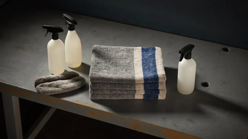Microfibres, gant de lavage et flacons neutres posés sur un établi en béton